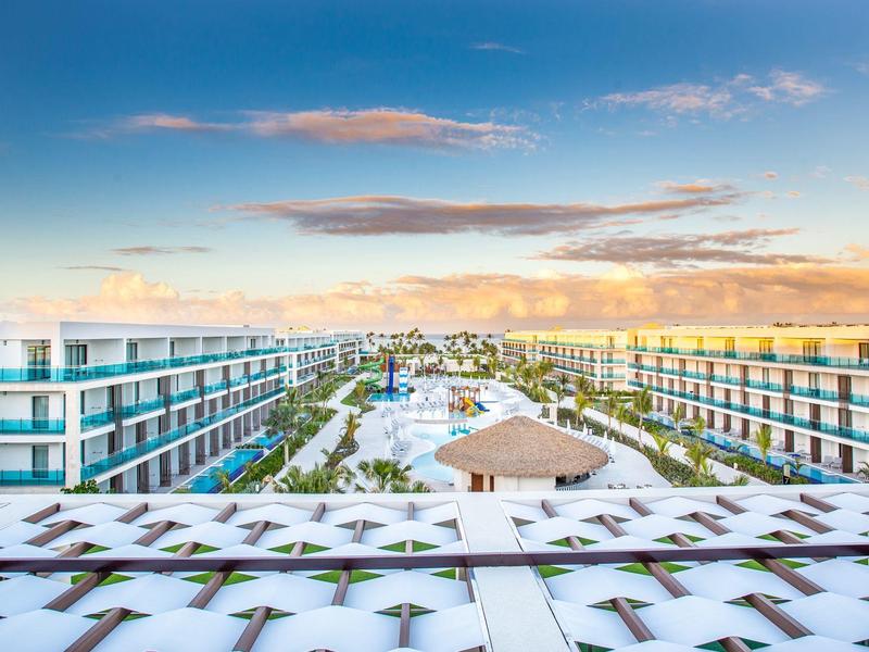 Uitzicht op een modern hotel met zwembad en tuinen bij zonsondergang.