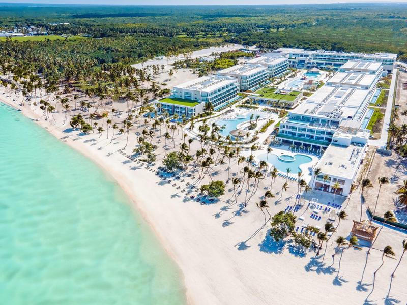 Groot resort met meerdere gebouwen op een wit zandstrand en turquoise water.