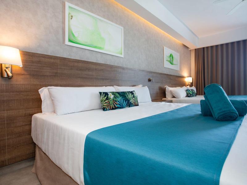 Modern ingerichte hotelkamer met groot bed, blauwe accenten en zachte wandverlichting.