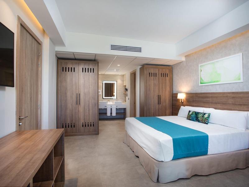 Moderne hotelkamer met groot bed, houten meubels en neutrale kleuren.