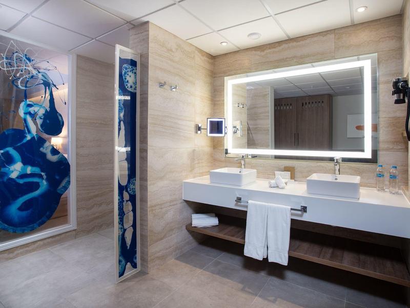 Moderne hotelbadkamer met verlicht spiegel, wastafel en douche met blauwe muurschildering.