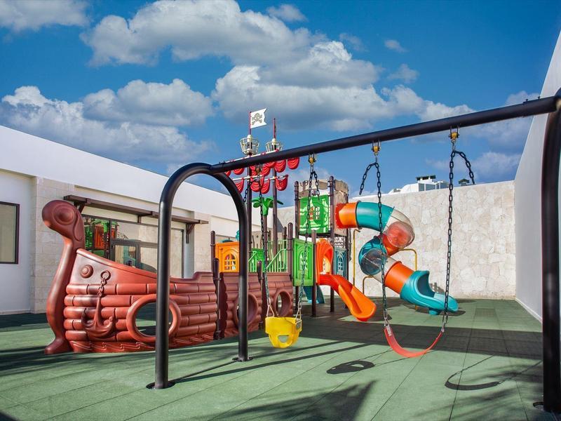Kinderspeelplaats met kleurrijke glijbanen en schommels op een dak onder een blauwe lucht.