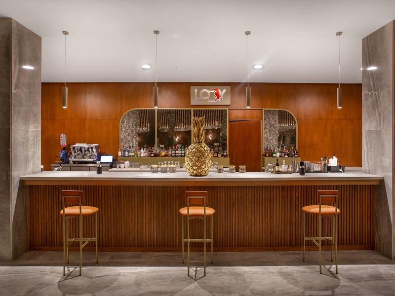 Elegante hotelbar met houten panelen, drie barkrukken en decoratieve spiegels aan de achterwand.