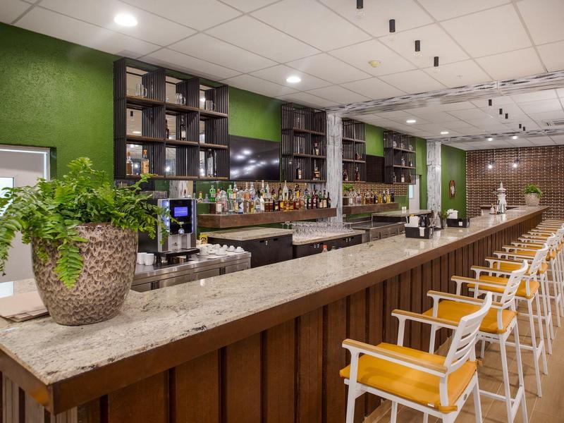 Moderne bar met lange marmeren toonbank, houten stoelen en groene muur in een hotel.