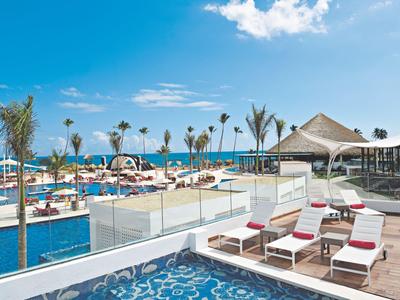 Espace piscine moderne avec transats, palmiers et vue sur la mer sous un ciel dégagé.