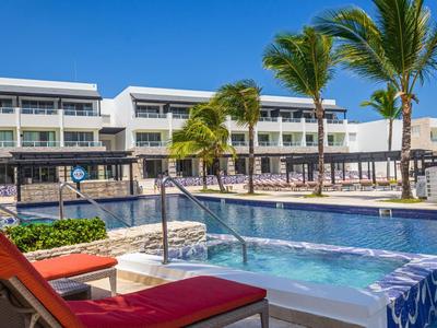 Außenwhirlpool mit roten Liegestühlen vor einem modernen Hotel unter blauem Himmel.