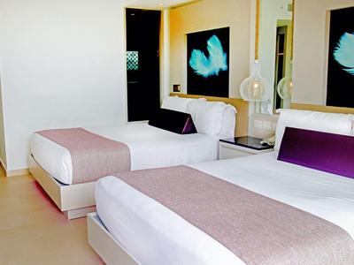 Modern eingerichtetes Hotelzimmer mit zwei weißen Betten und lila Akzenten.