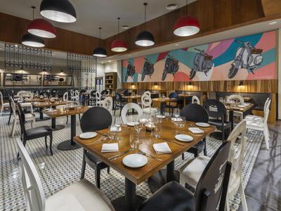 Modernes Restaurant mit elegant gedeckten Tischen, Stühlen in Schwarz und Weiß und buntem Wandbild.