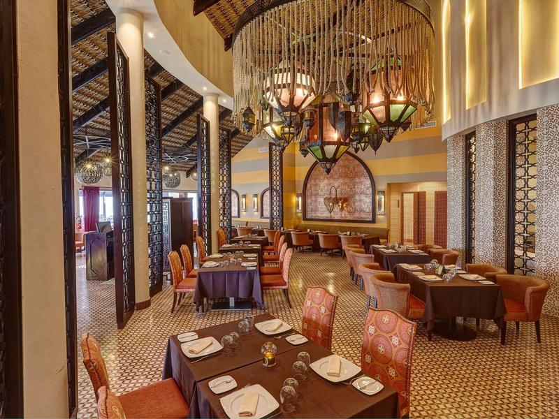 Elegantes Restaurant mit braunen Tischen, roten Stühlen und kunstvollen Pendelleuchten.