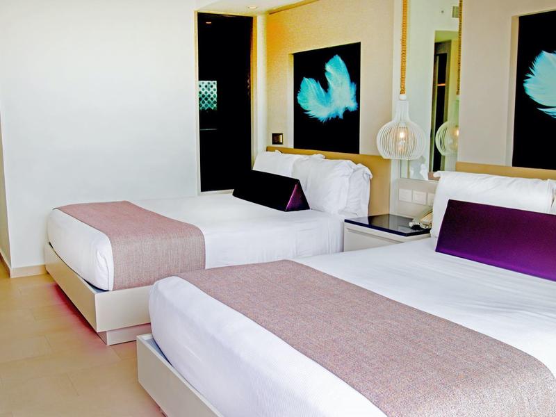 Modern eingerichtetes Hotelzimmer mit zwei weißen Betten und lila Akzenten.