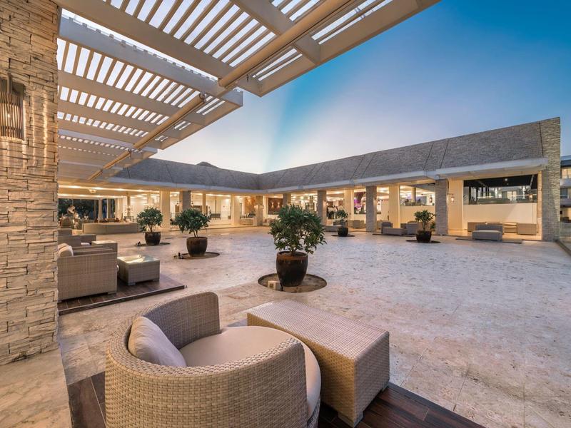 Innenhof eines Hotels mit Sitzbereichen unter einem Pergoladach bei Sonnenuntergang.