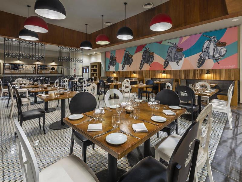 Modernes Restaurant mit elegant gedeckten Tischen, Stühlen in Schwarz und Weiß und buntem Wandbild.