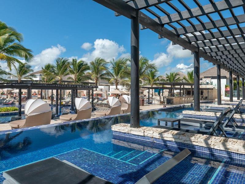 Moderner Poolbereich mit Barsitzgelegenheiten und Palmen unter blauem Himmel