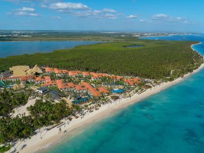 Vista aerea di una località balneare tropicale con bungalow, spiaggia di sabbia bianca e mare blu.