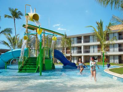Bambini che giocano in un parco acquatico davanti a un hotel in una giornata di sole.