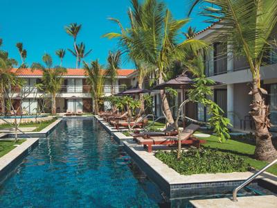 Moderní hotelový bazén obklopený palmami a lehátky za slunečného počasí.