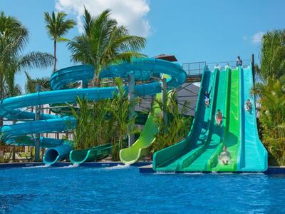 Parco acquatico con scivoli d'acqua e piscina, circondato da palme e cielo sereno.