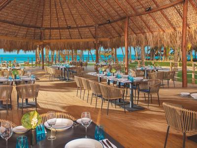 Ristorante tropicale aperto con tavoli apparecchiati e vista sul mare.