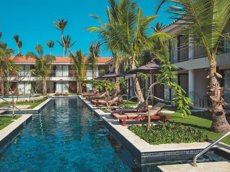 Piscina moderna dell'hotel con lettini e palme in un ambiente tropicale.