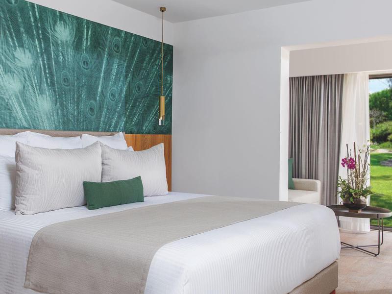 Camera d'hotel moderna con letto grande, decorazione murale verde e vista sul giardino.