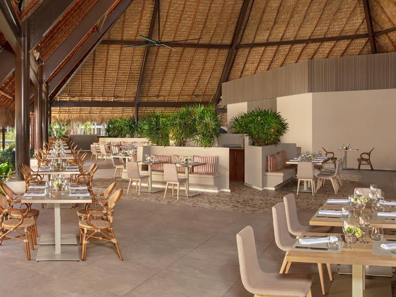 Area ristorante moderna all'aperto con mobili in legno e tetto in paglia in un hotel.