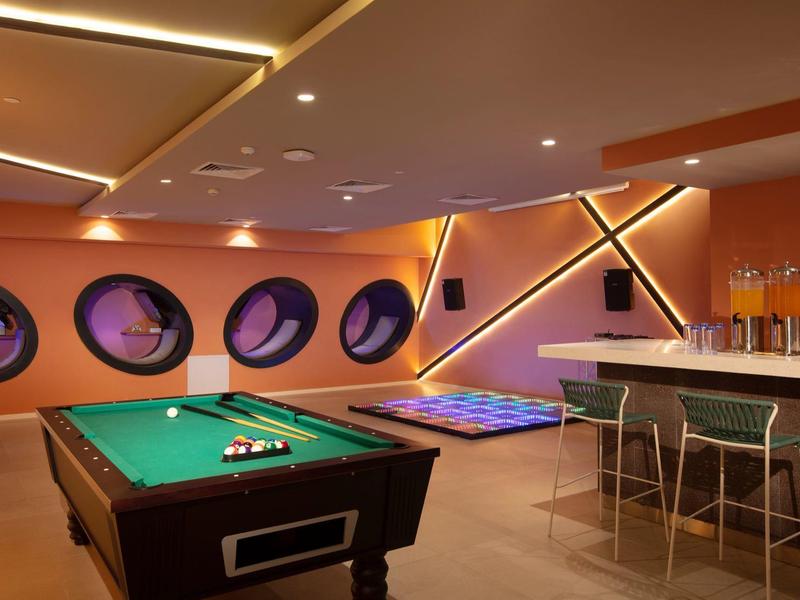 Sala giochi moderna con tavolo da biliardo, sgabelli da bar e oblò rotondi.