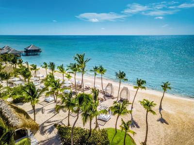 Strand mit Palmen, Liegestühlen und klarem blauem Meer unter bewölktem Himmel.