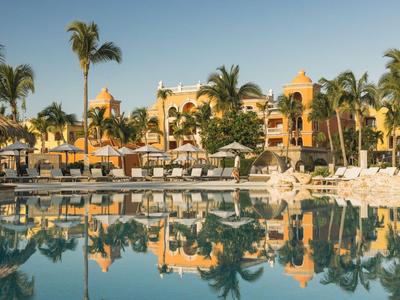 Hotel de lujo con palmeras y gran piscina al atardecer.