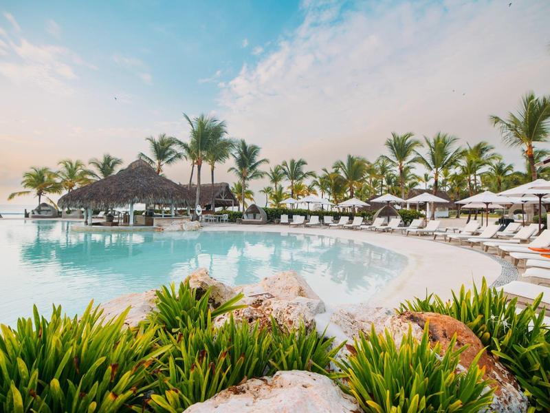 Groot hotelzwembad met parasols en palmbomen in een tropisch resort.