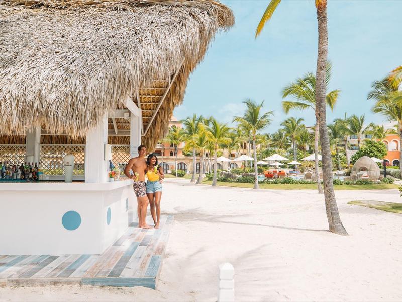 Twee vrouwen staan onder een palmbladdak bij een strandbar in een tropisch resort.