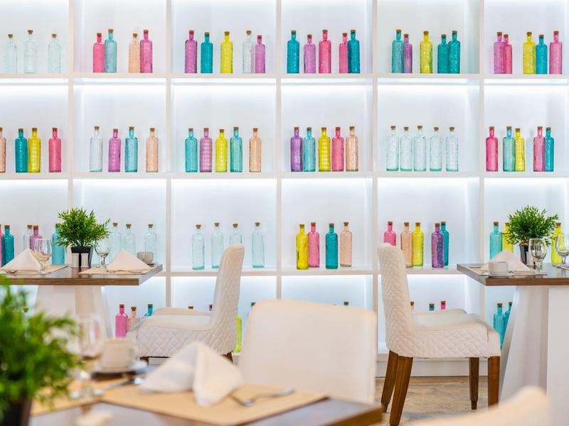 Modern restaurant met kleurrijke waterflessen en witte meubels.