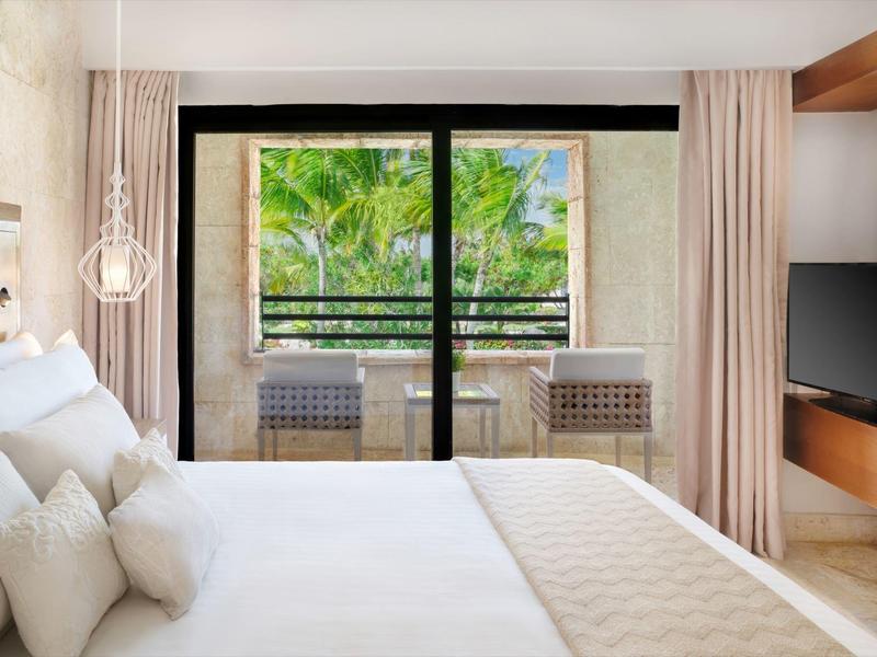 Lichte hotelkamer met tweepersoonsbed, balkon en uitzicht op palmbomen.