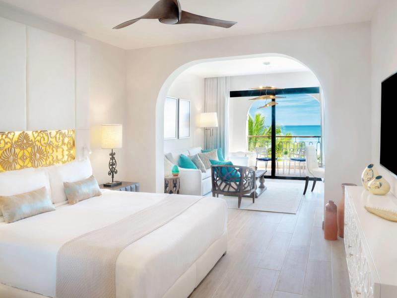 Lichte hotelkamer met twee bedden, plafondventilator en zeezicht vanaf het balkon.