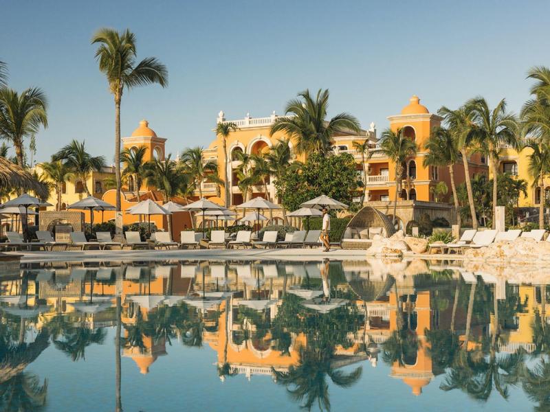Luxe hotelcomplex met zwembad, ligstoelen en palmbomen bij zonsondergang.