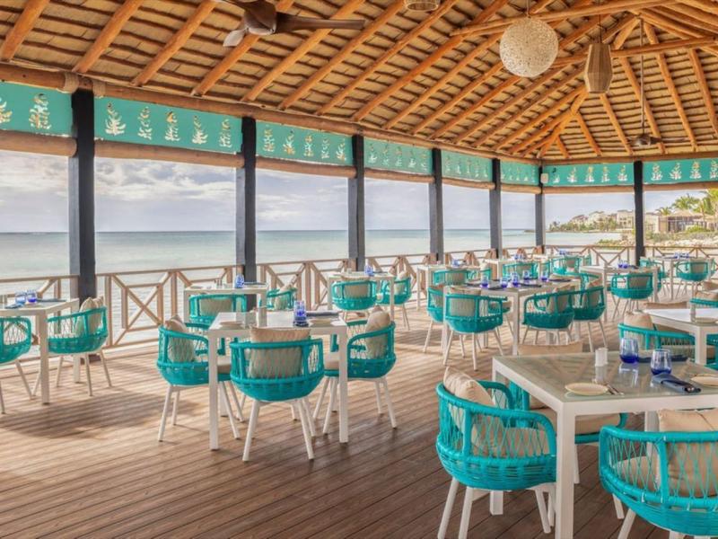 Overdekt terras met blauw gevoerde stoelen en tafels met uitzicht op water en landschap.