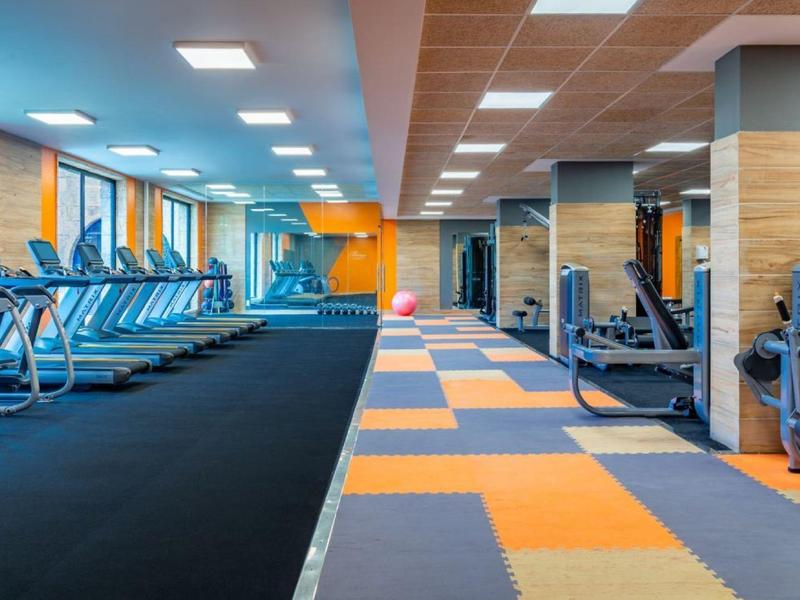 Moderne fitnessruimte met loopbanden, trainingsapparatuur en kleurrijke vloerbedekking.