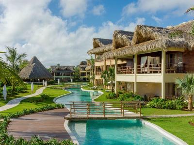 Luxury hotel resort with swimming pool, bridges, and tropical vegetation under cloudy sky.