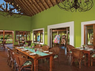 Gemütlicher, grüner Speiseraum mit Holzmöbeln und Blick auf Garten und Schwimmbad.