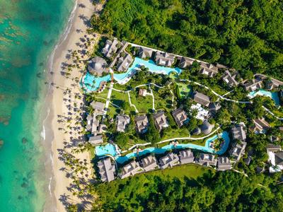 Complesso alberghiero con più piscine e accesso diretto a una spiaggia di sabbia vicino a rigogliosa vegetazione.