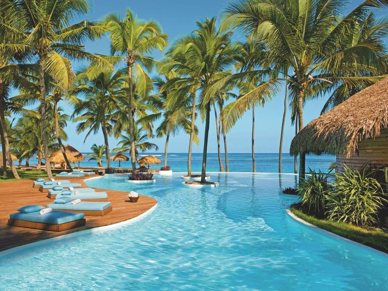 Ein tropischer Poolbereich mit Palmen, Sonnenliegen und Blick auf das Meer.