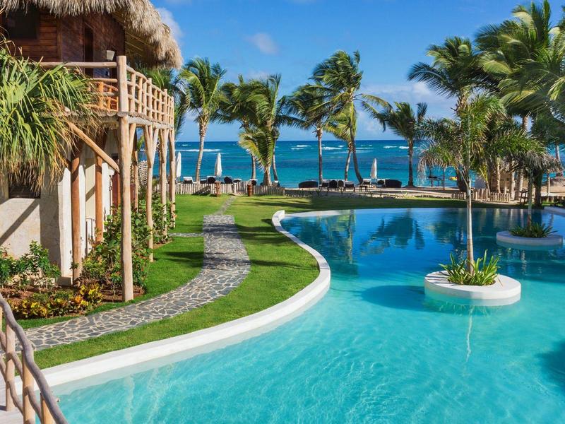 Ein tropischer Poolbereich mit Palmen und Blick auf das Meer bei klarem Himmel.