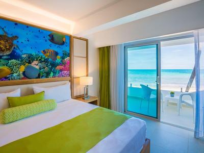 Helles Zimmer mit großem Bett, grüner Bettdecke, Meeresblick und buntem Bild über dem Kopfteil.