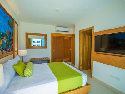 Modernes Schlafzimmer mit Doppelbett, grüner Bettwäsche, Wandbild, TV und Holzfronten.