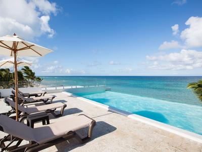 Infinity-Pool mit Liegestühlen und Sonnenschirm mit Blick auf das Meer unter blauem Himmel.