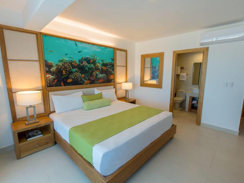 Modernes Schlafzimmer mit großem Bett, grün-weißer Bettwäsche, Holzrahmen und Meeresbild an der Wand.