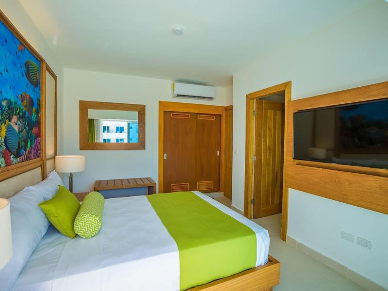 Modernes Schlafzimmer mit Doppelbett, grüner Bettwäsche, Wandbild, TV und Holzfronten.