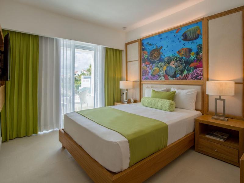 Hell eingerichtetes Schlafzimmer mit großem Bett, grün-weißer Bettwäsche und farbenfrohem Wandbild.