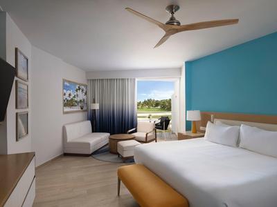 Modern hotel room with large bed, blue accent wall, and seating area with a view.