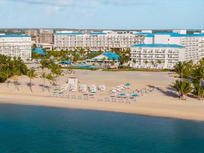 Beachfront hotel with lounge chairs and palm trees by the blue sea.