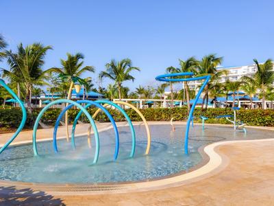 Children's splash pool with water arches and palm trees in the background on a sunny day.